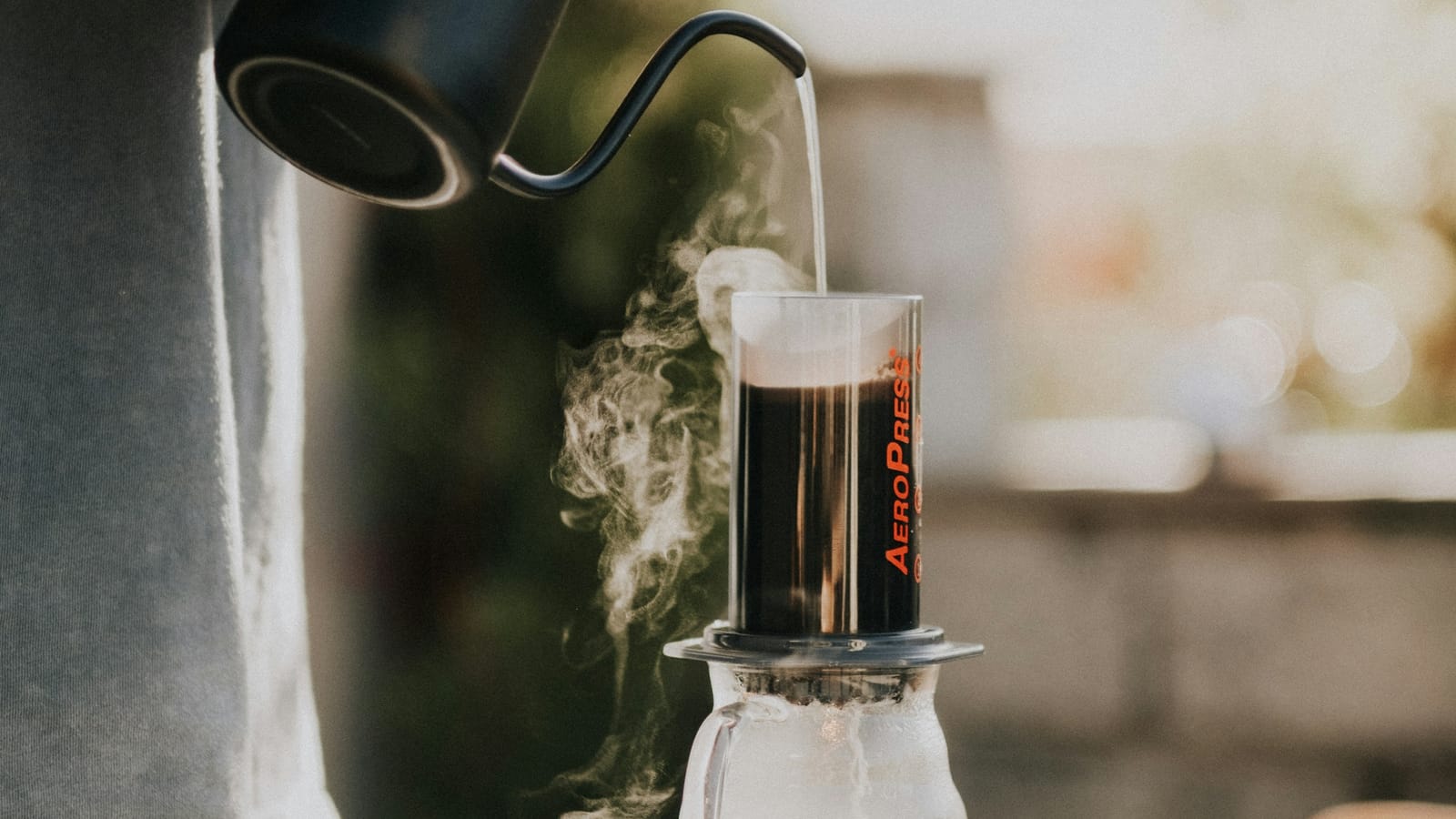 Chaleira de bico fino despejando água quente em uma AeroPress apoiada sobre uma jarra de vidro