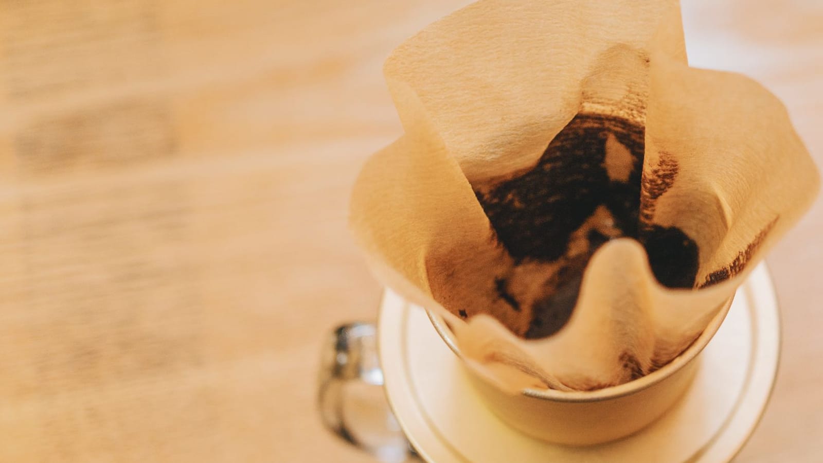 Filtro de papel pardo com café, encaixado em um porta-filtro sobre uma caneca de vidro