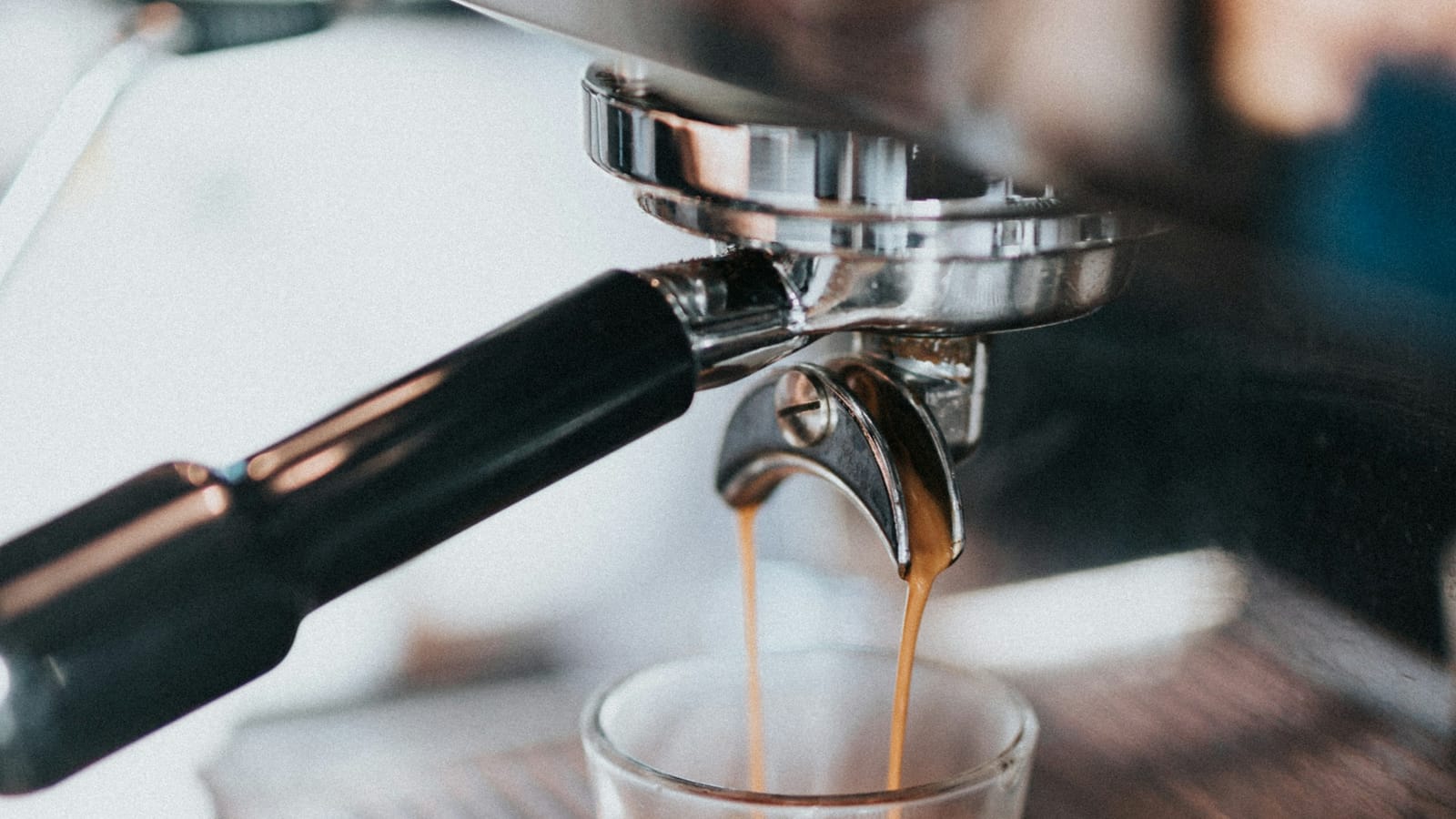 Espresso escorrendo do porta-filtro de uma máquina para um copinho de vidro