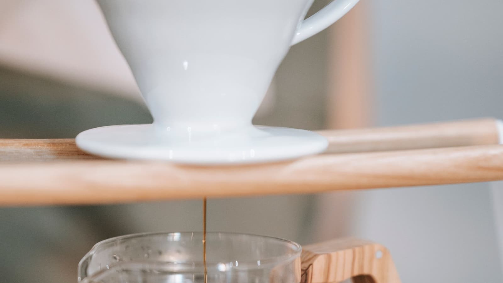 Dripper de cerâmica branca sobre suporte de madeira, com um fio de café escorrendo para uma jarra de vidro (foto ilustrativa de café coado, não é o Hario Switch)