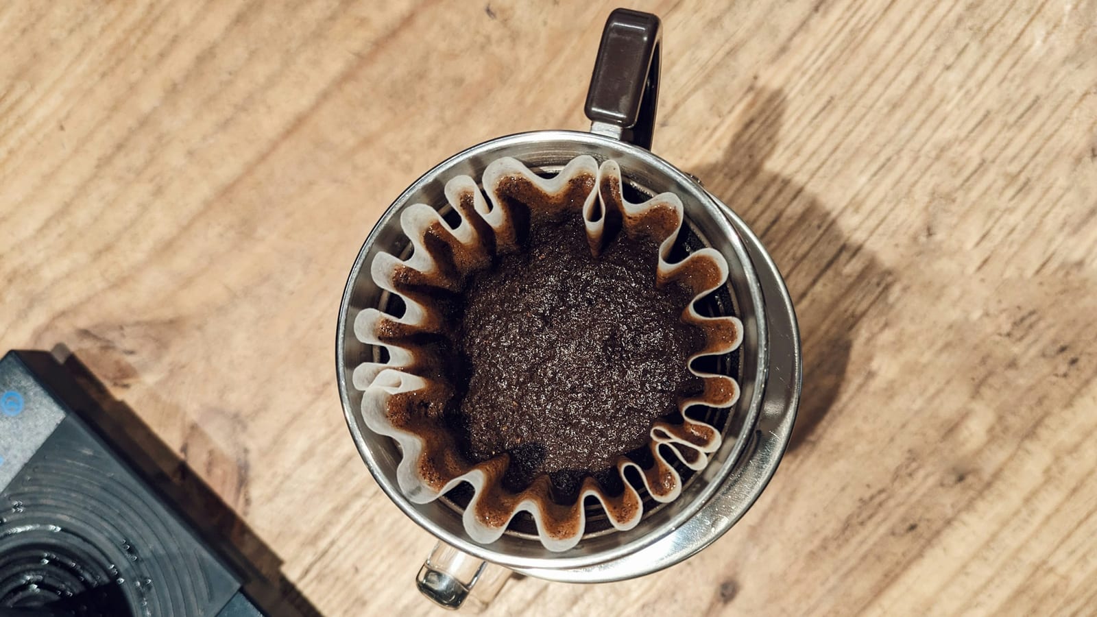 Café moído em um filtro de papel ondulado do tipo Kalita Wave, visto de cima, sobre uma mesa de madeira