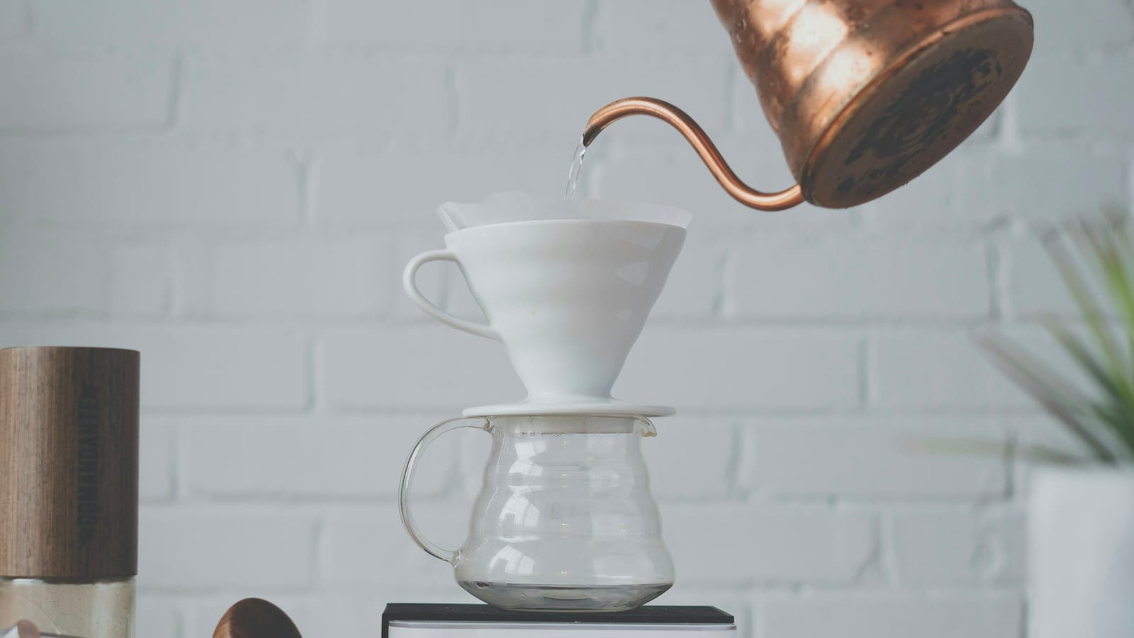 Chaleira de cobre de bico fino despejando água em um dripper V60 branco sobre uma jarra de vidro