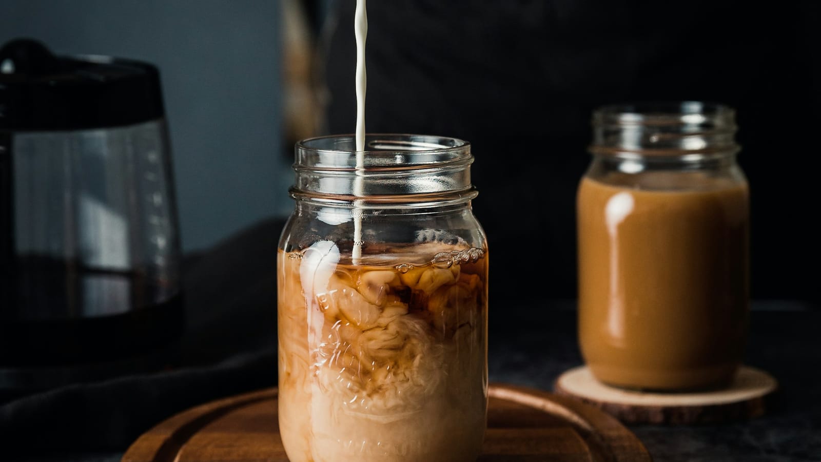 Leite sendo despejado em um pote de vidro com café gelado e cubos de gelo