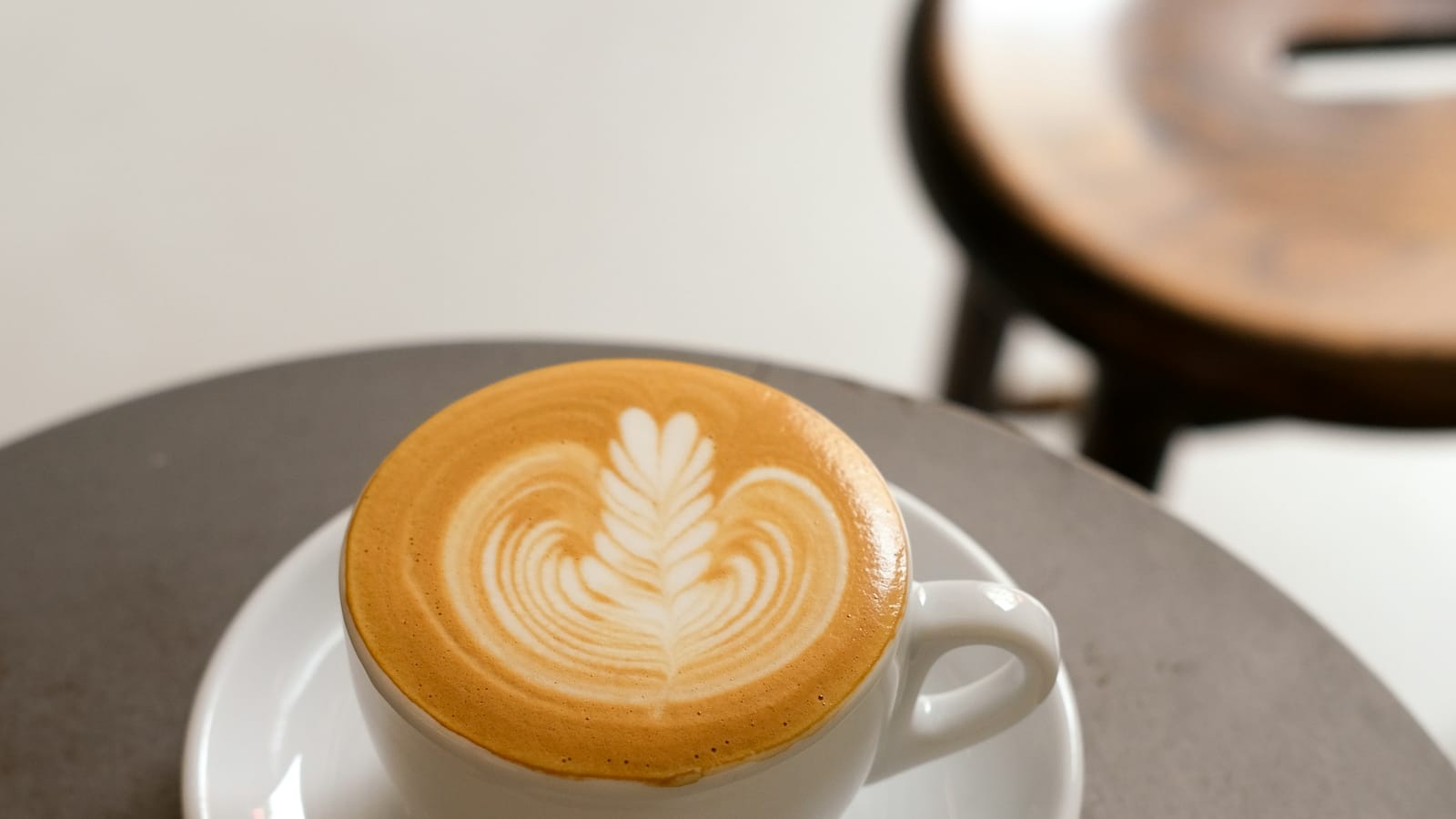 Xícara branca com café e leite e desenho de folha na espuma, sobre pires
