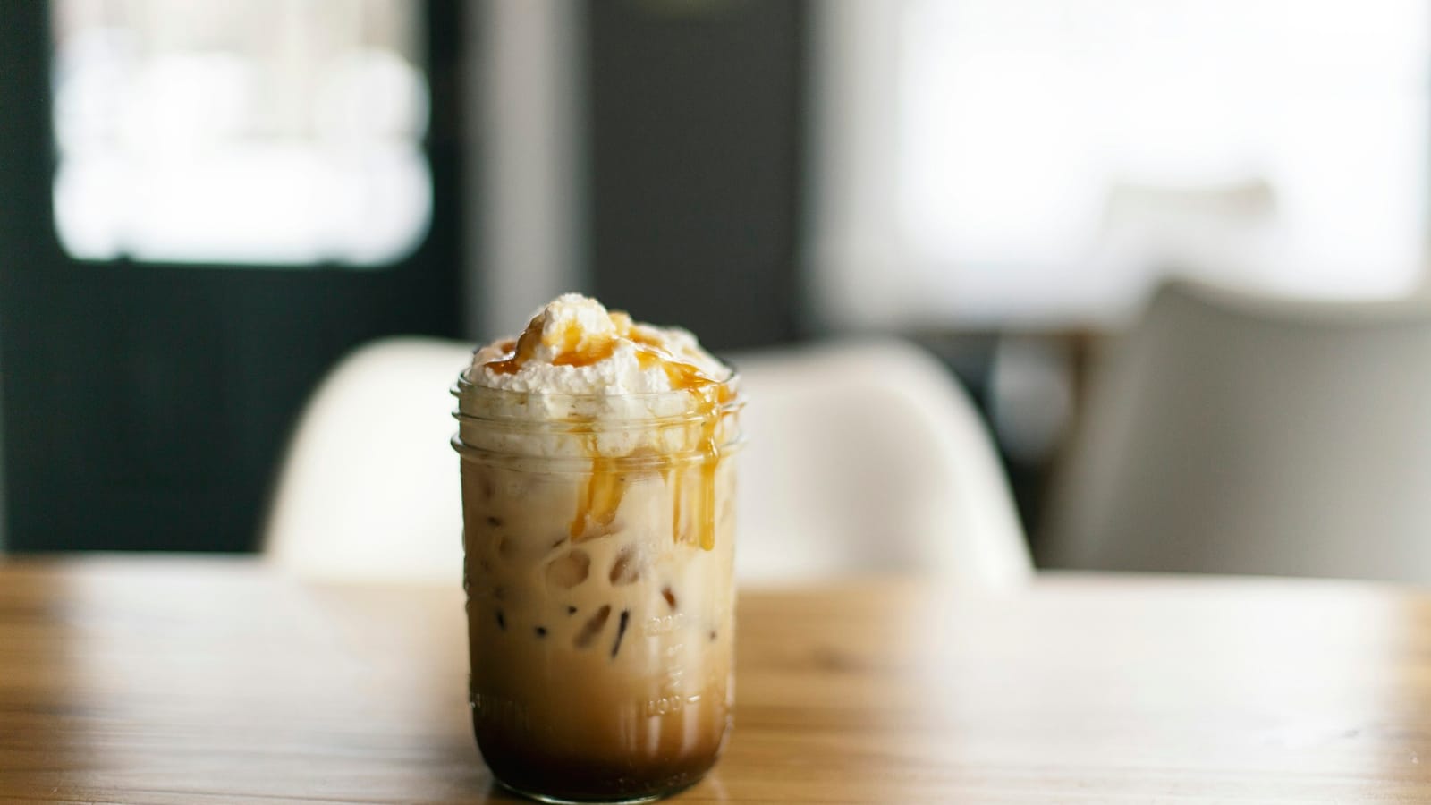 Copo de vidro com frappé de café, chantili e calda de caramelo, sobre mesa de madeira