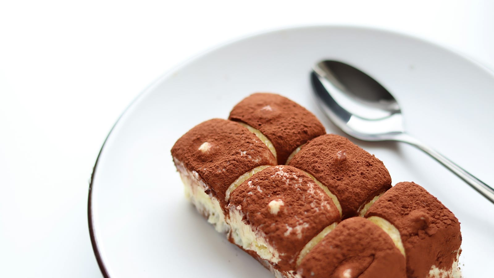 Fatia de tiramisù polvilhada com cacau em prato branco, com colher